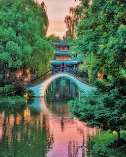 Arched bridge over a canal in a leafy garden with pavilion and water reflections