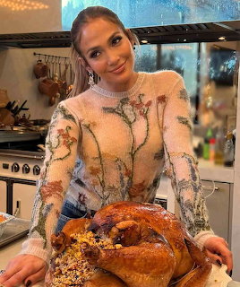 Smiling woman in white floral dress presenting braided bread in kitchen