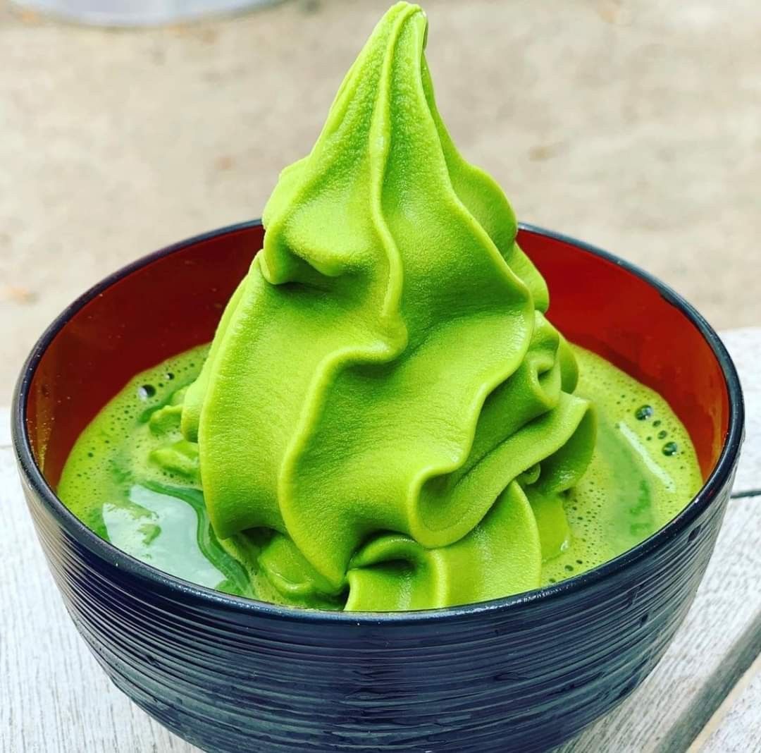 Swirled green matcha soft serve ice cream in a black bowl with red interior