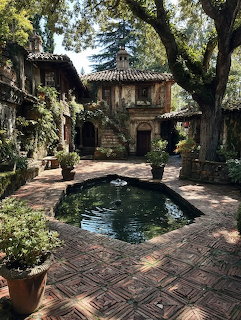 Rustic courtyard with stone fountain, brick pavement, aged buildings and trees