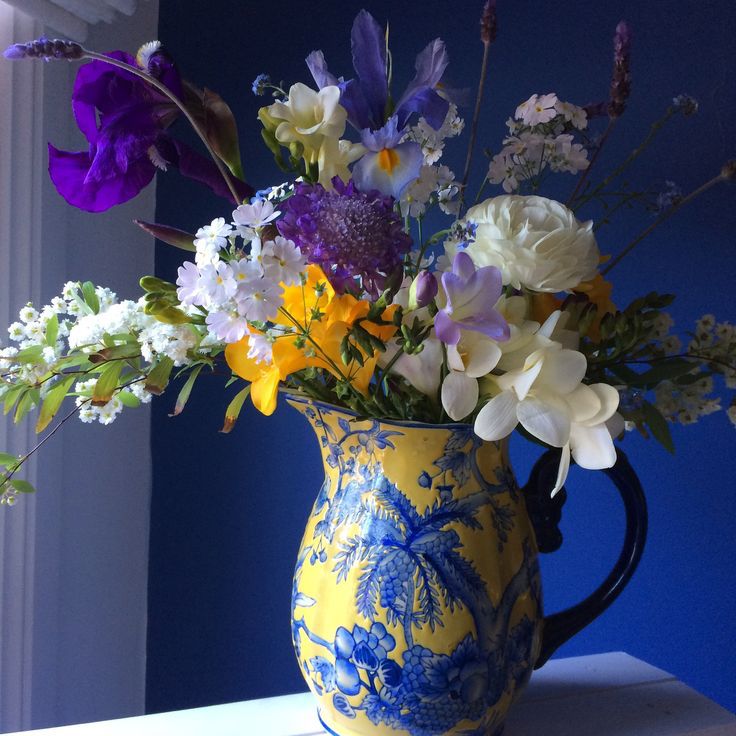 Vibrant wildflower arrangement in ornate blue and yellow pitcher on dark blue background
