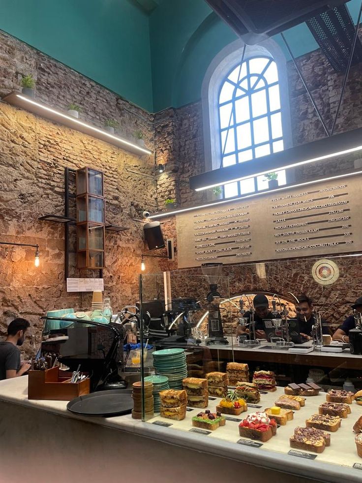 Cafe interior with pastry display counter, exposed brick walls, turquoise vaulted ceiling, arched window