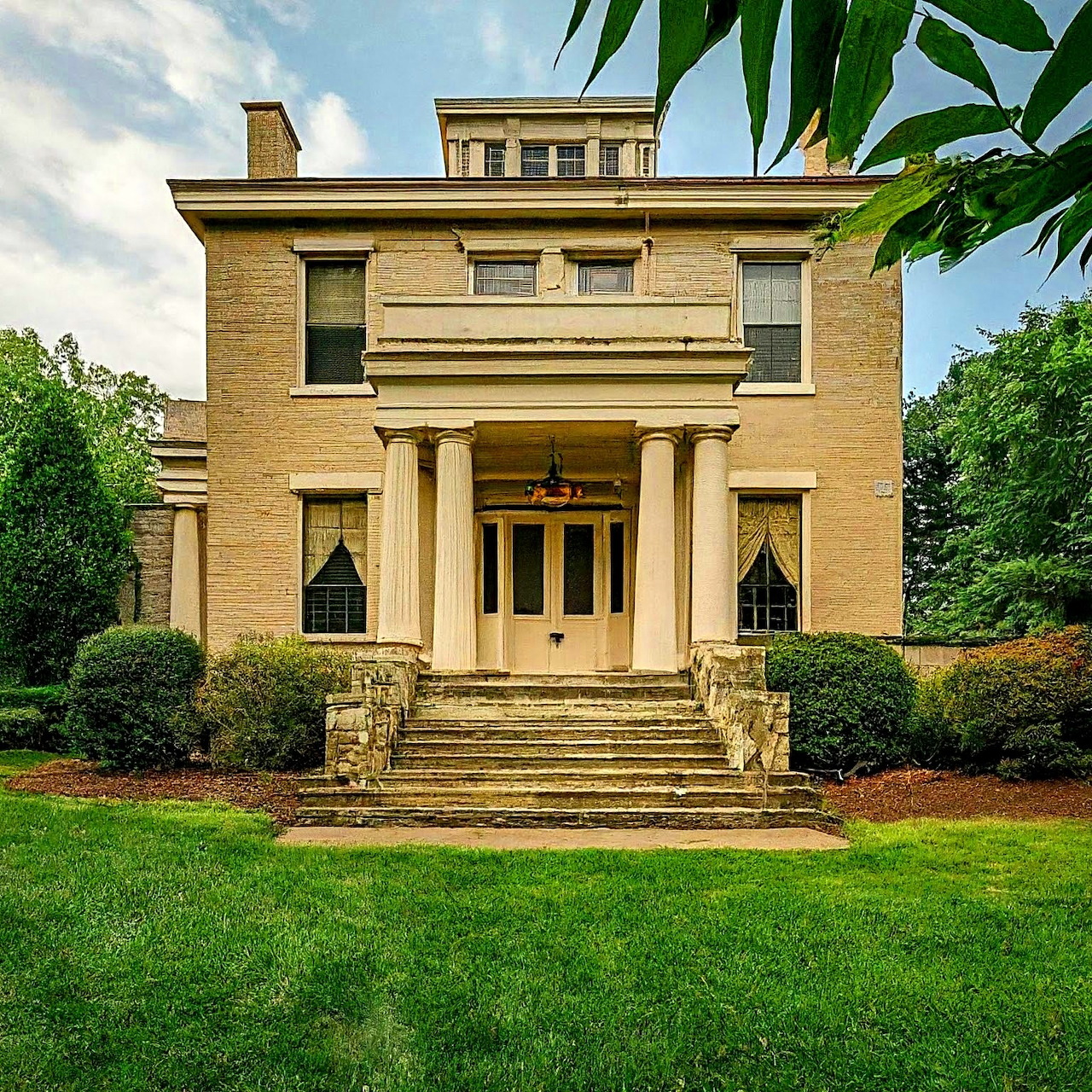 Yellow Greek Revival style mansion with columned portico and stone steps on green lawn
