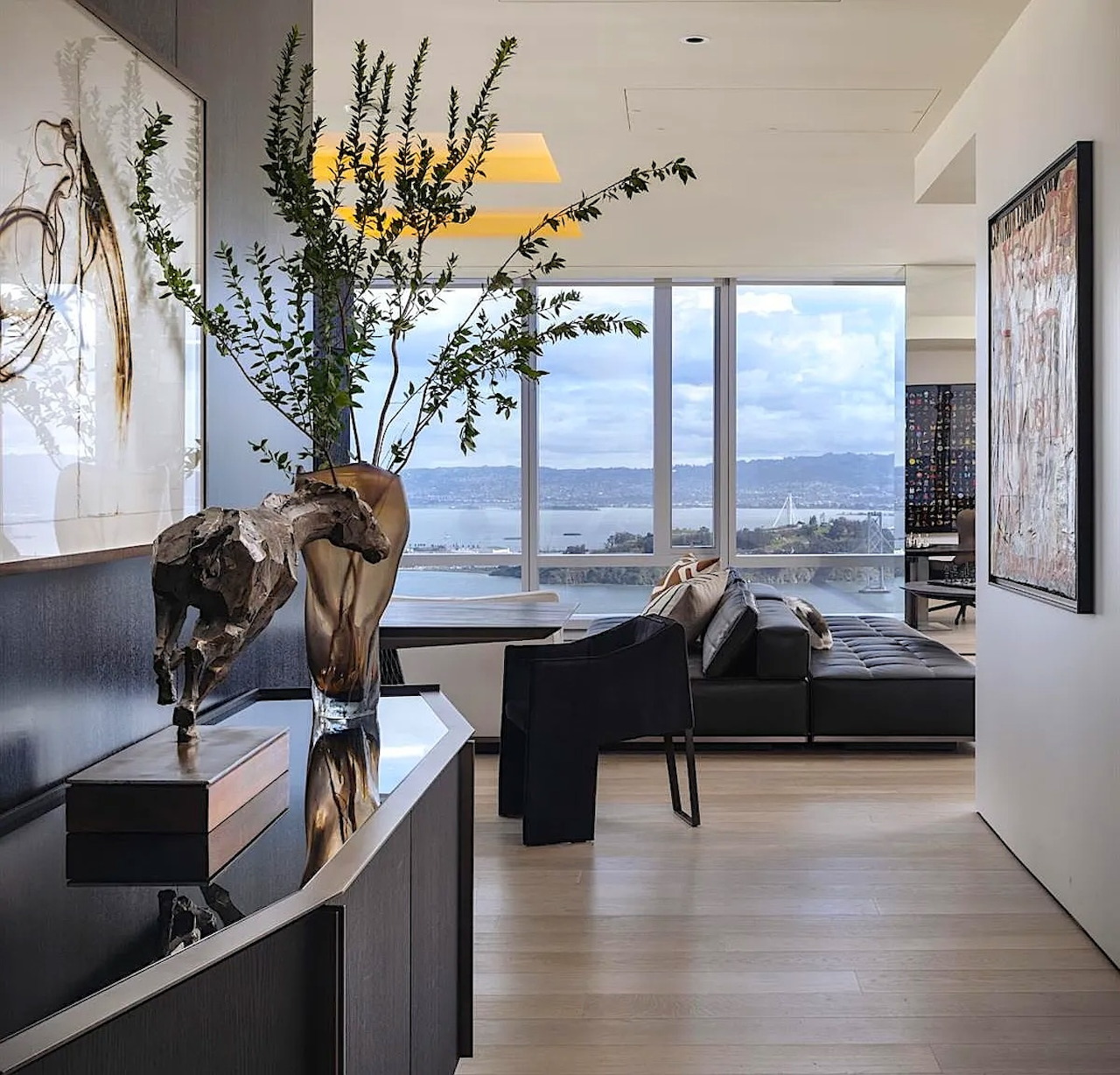 Modern living room with panoramic ocean view, black sofa, wood floors, and tall decorative branches