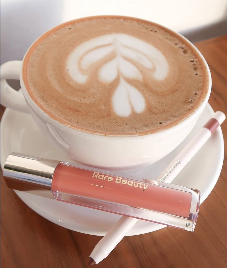 Latte with leaf art next to lip gloss tube and lip pencil