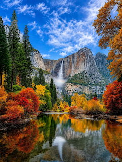 Yosemite Falls with autumn colored trees reflected in the Merced River under a blue sky