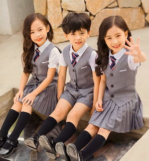 Three young children in grey school uniforms sitting together on stone steps, smiling at the camera