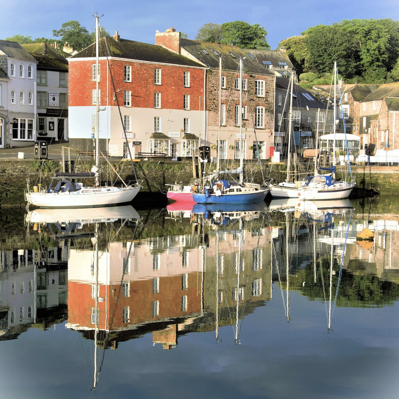 Sailboats in Padstow harbour with waterfront buildings reflected in calm water