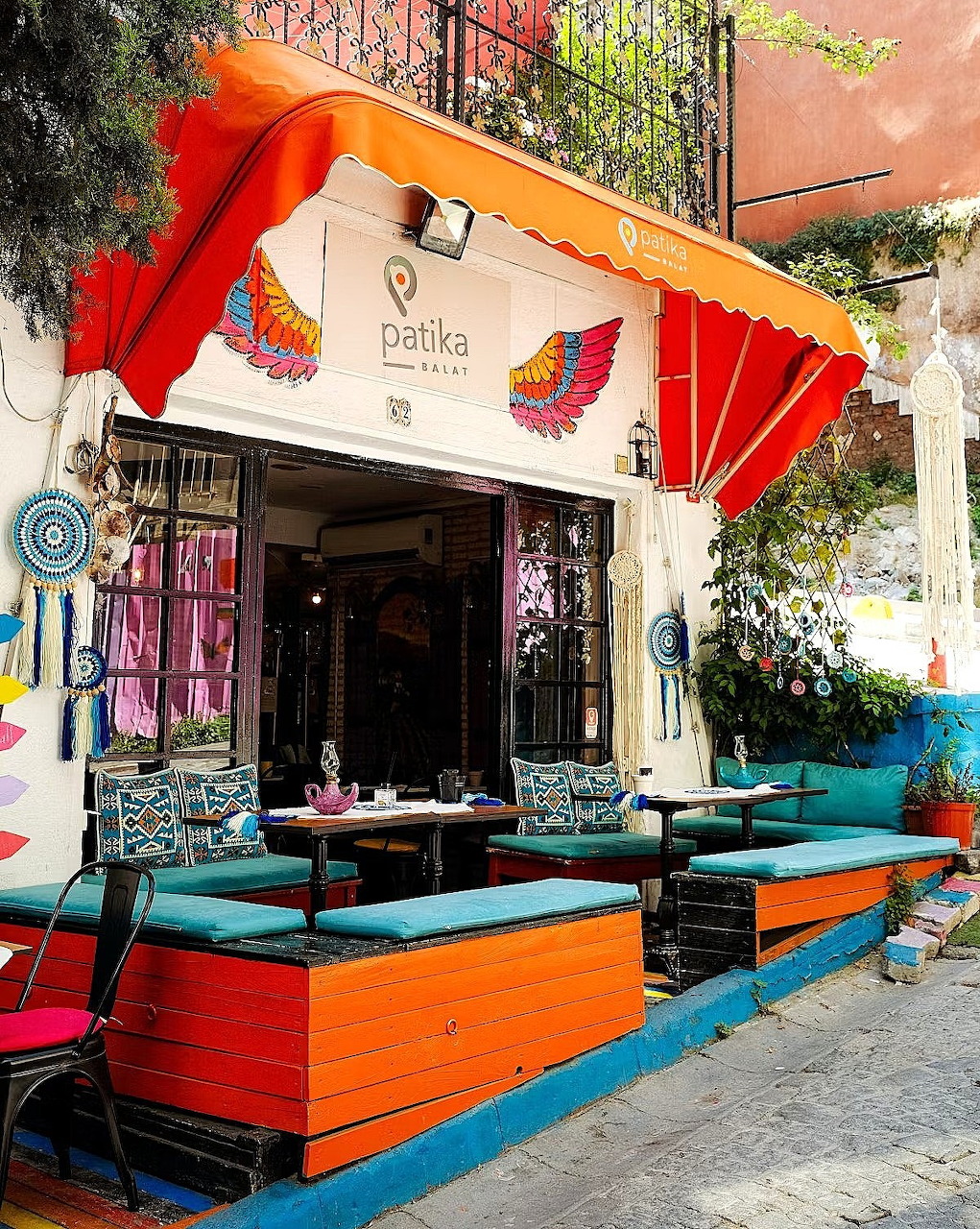 Colorful cafe storefront with orange awning, painted murals, and turquoise outdoor seating on sunny sidewalk