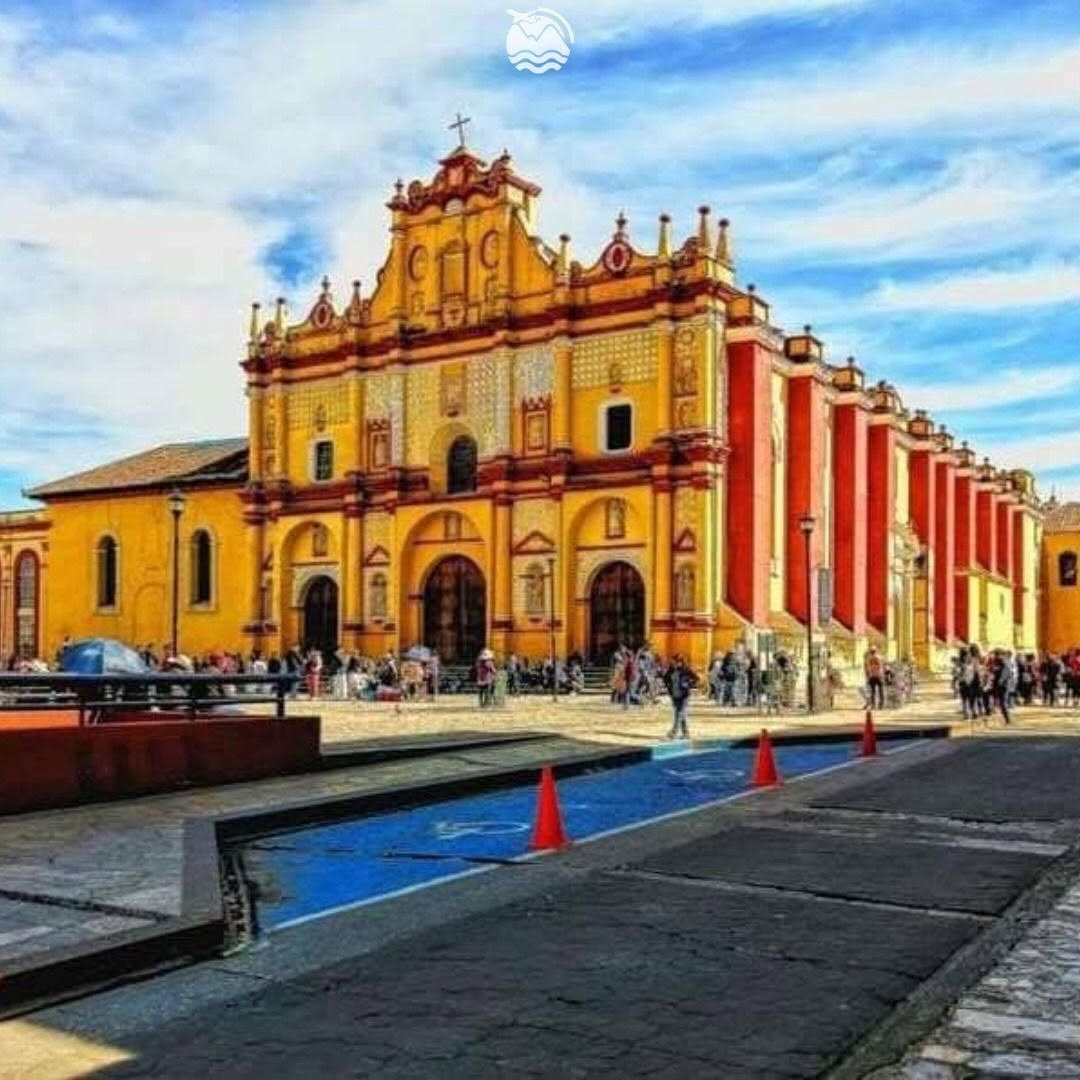 Yellow colonial church with red trim beside a street under a blue sky