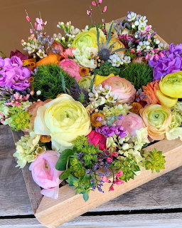 Colorful mixed flower arrangement in wooden box with ranunculus, roses, carnations and greenery