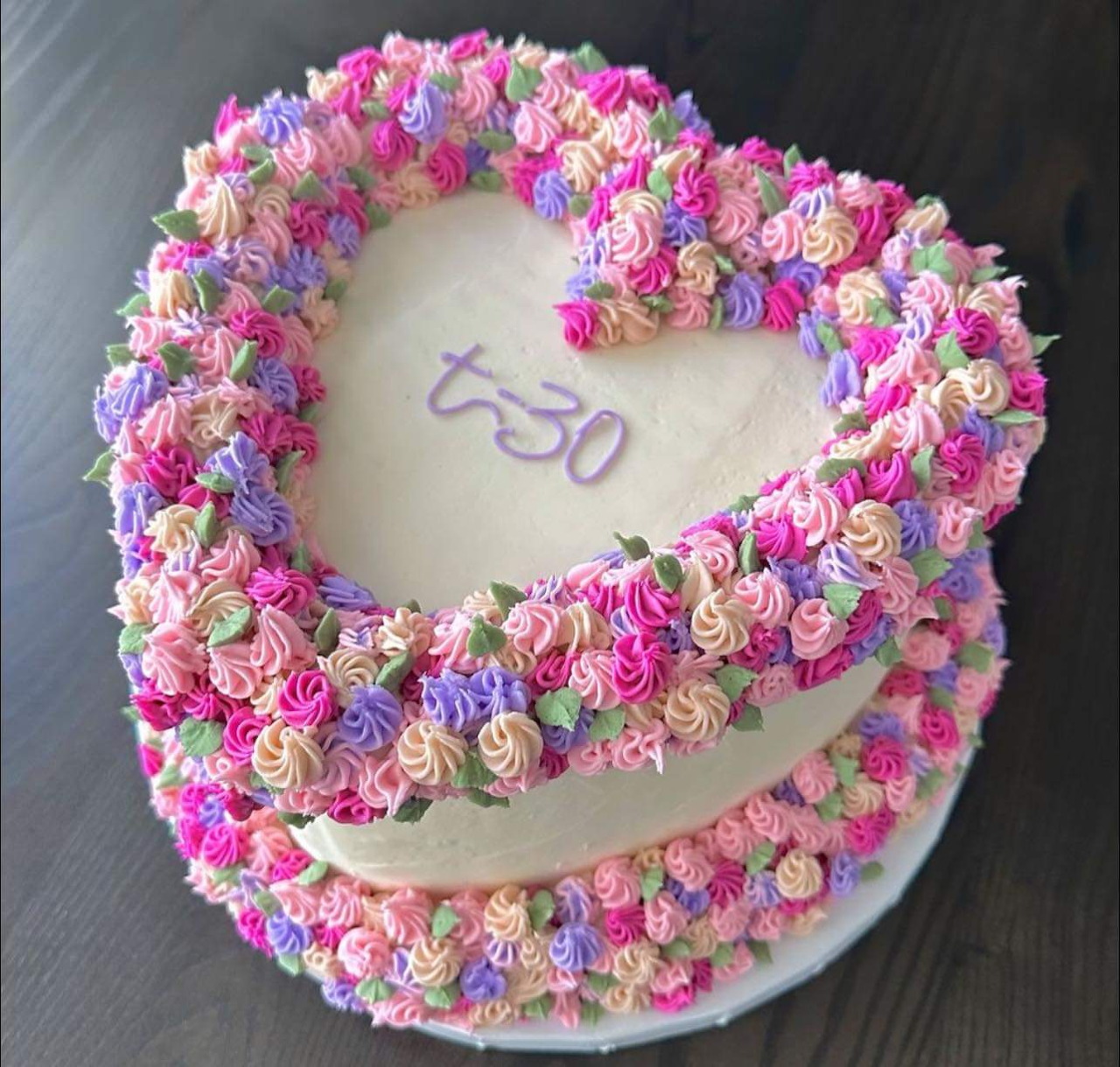 Heart-shaped cake with colorful frosting flowers covering two tiers