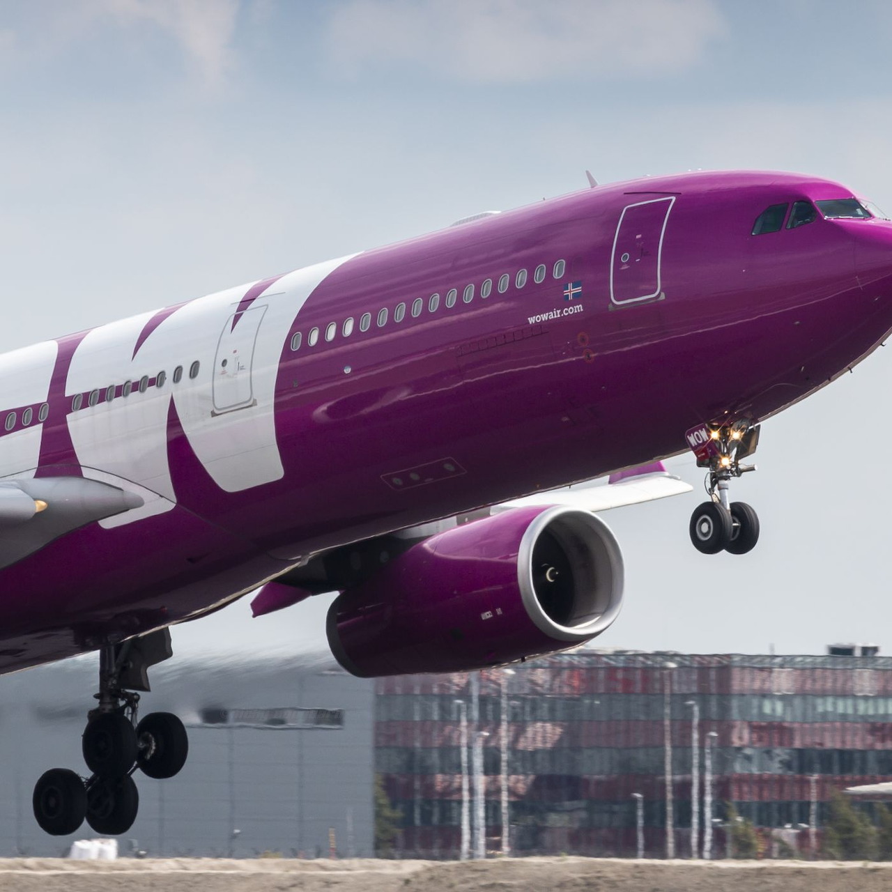 Purple passenger airplane landing with gear down near airport buildings