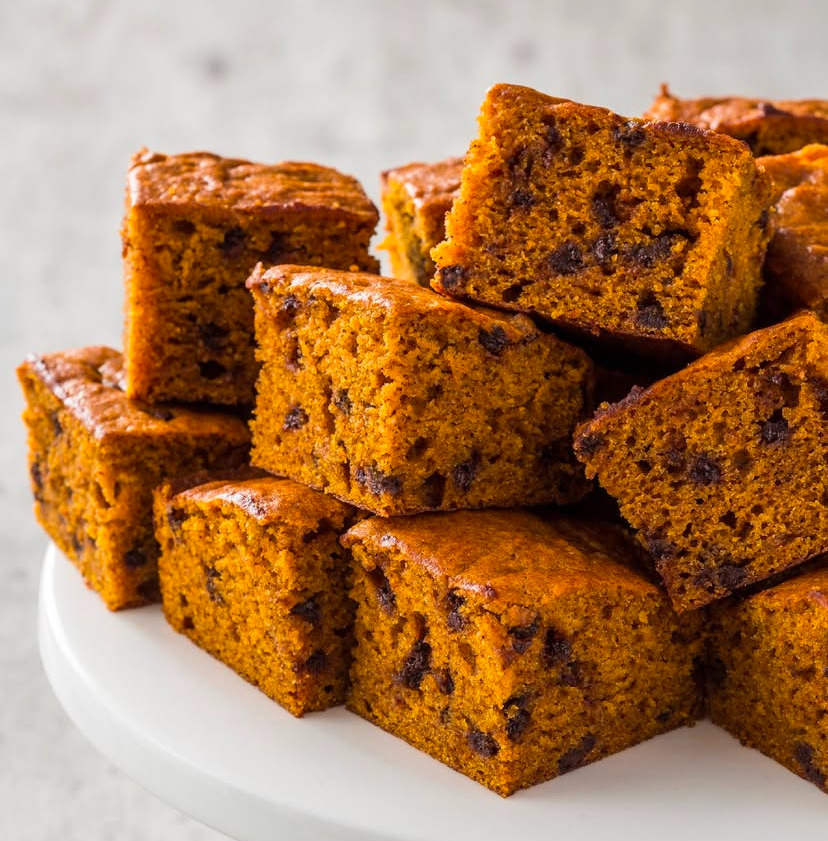 Stacked spiced cake squares with dark fruit pieces on a white plate