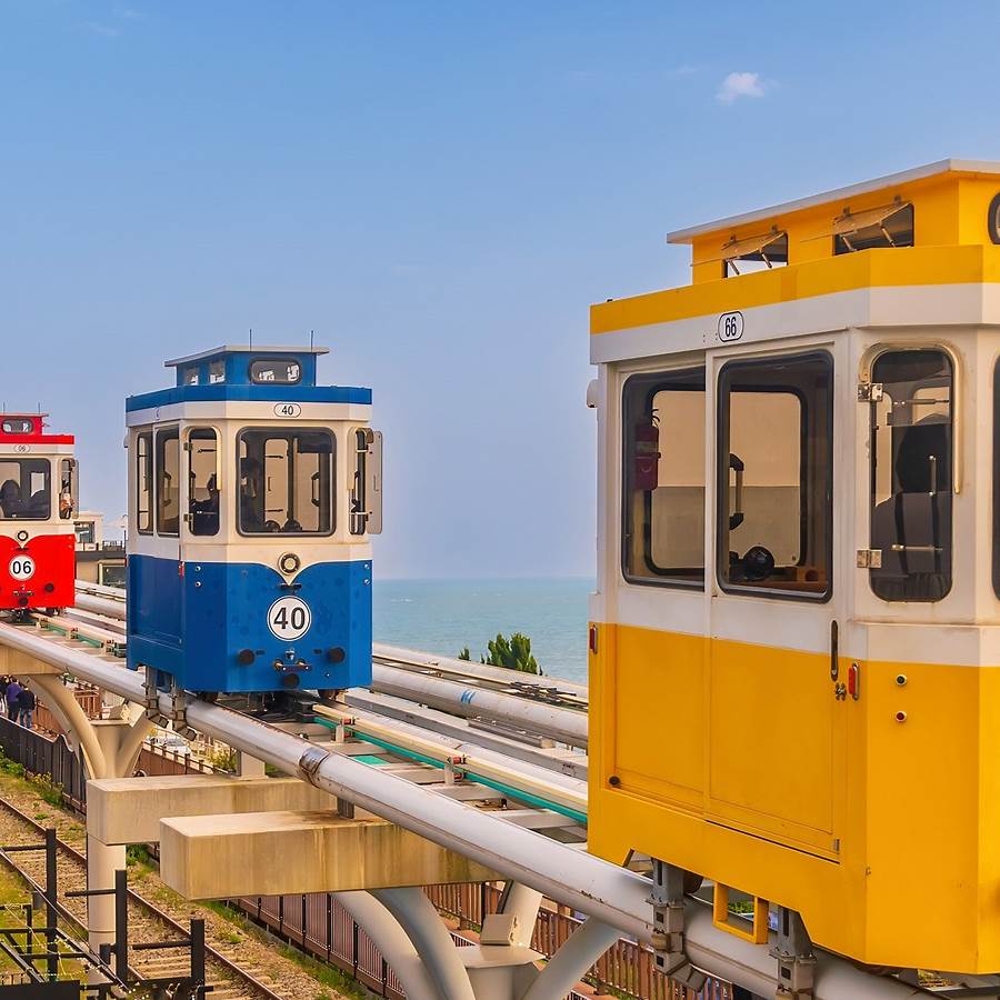 Colorful sky capsule cars on elevated monorail track with ocean in background in Busan South Korea