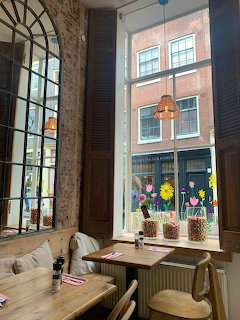 Small cafe seating area by tall windows with flower vases and a brick building outside