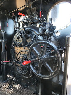 Interior view of vintage steam locomotive cab with controls, gauges, and large mechanical wheel