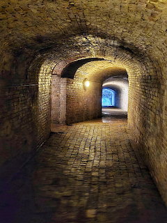 Dim brick underground passage with arched ceiling and cobblestone floor