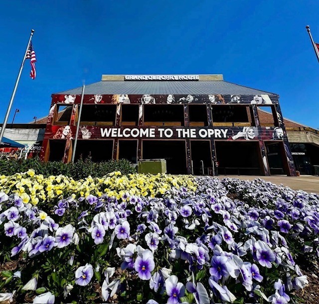 Grand Ole Opry building entrance with yellow and purple flower garden and American flags