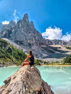 Person sitting on rock at turquoise mountain lake with jagged peaks