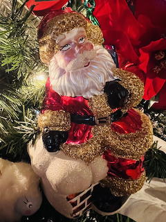 Glittery Santa ornament on a Christmas tree with red flowers and white lights