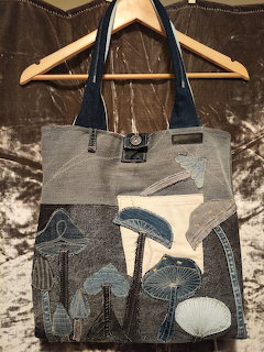Handmade denim patchwork tote bag with recycled jean pockets hanging on wooden hangers against crushed velvet background