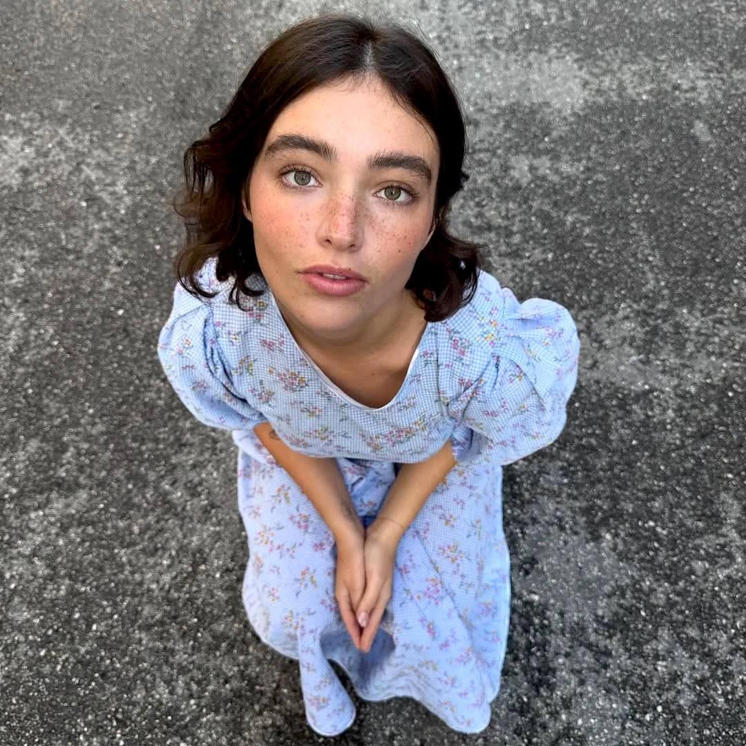 Overhead view of a young woman in a light blue floral dress looking up while standing on pavement.