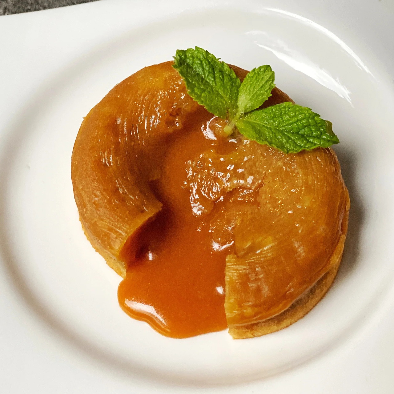 Golden lava cake drizzled with caramel sauce and garnished with mint on white plate