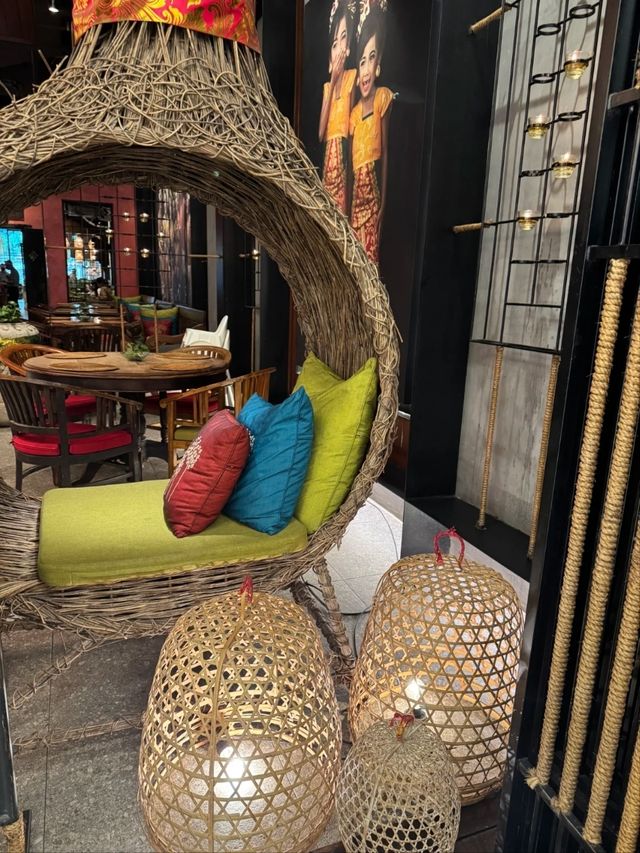 Large woven rattan hanging chair with colorful cushions and bamboo pendant lamps in a Balinese restaurant entrance