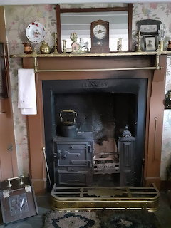 Traditional cast iron range fireplace with wooden mantelpiece holding clock and brass ornaments in a cottage interior