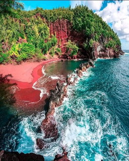 Red sand beach with green tropical cliffs and turquoise ocean waves crashing on volcanic rocks