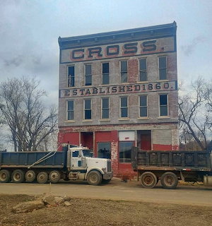 Old brick building with Cross signage from 1860 and white dump truck in front
