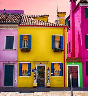 Colorful yellow, pink, and magenta houses with blue shutters in Burano, Italy under a pink sky