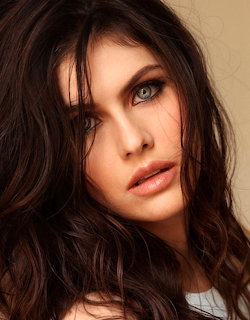 Close-up portrait of a woman with blue-green eyes and dark wavy hair