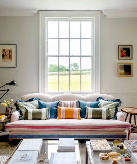 Colorful striped sofa with decorative cushions beneath a tall white-framed window in a bright living room