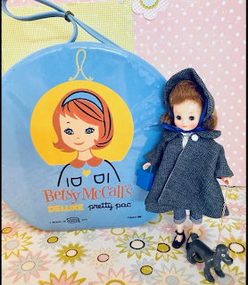Vintage Betsy McCall doll in blue cape next to round blue carrying case and small black dog figurine