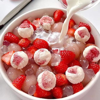 Overhead view of a white bowl filled with strawberries, lychee jelly balls, and tapioca pearls in milk