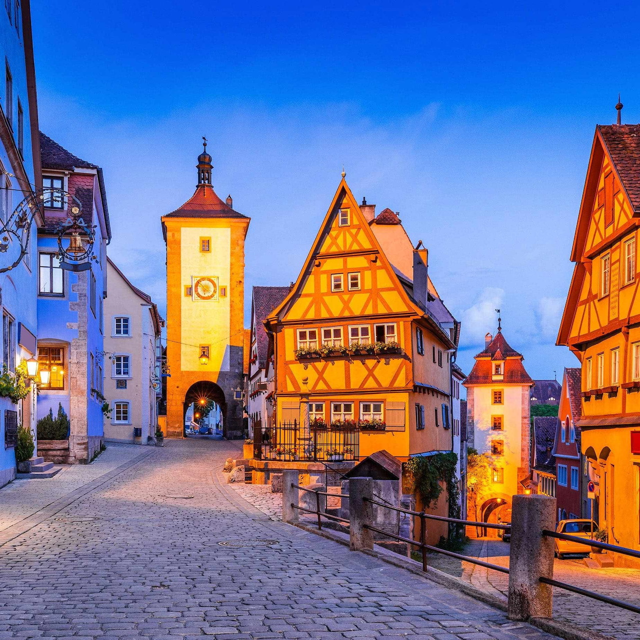 Cobbled street with glowing half-timbered houses and towers in an old European village at dusk
