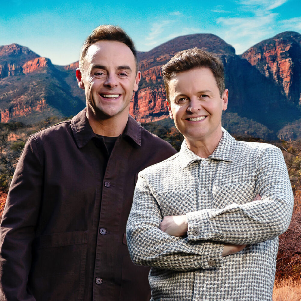 Two men smiling at camera with dramatic mountain landscape behind them
