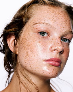 Close-up portrait of woman with freckles and blue eyes looking at camera