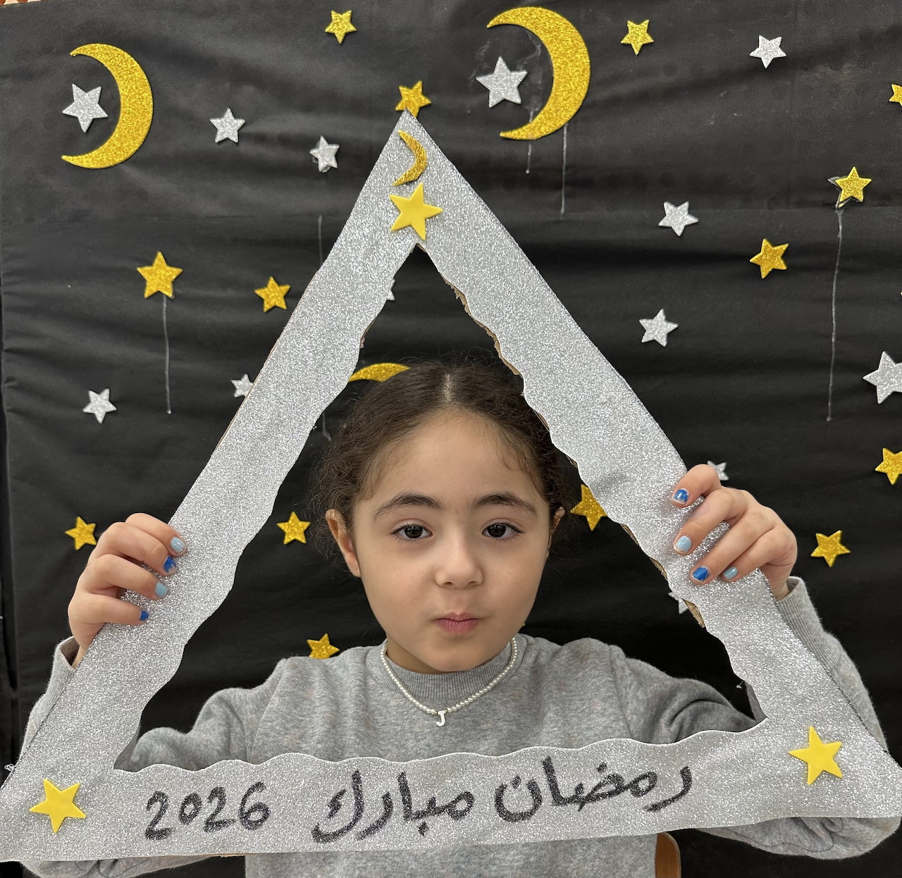 Young girl holding a Ramadan greeting frame against a moon and stars backdrop
