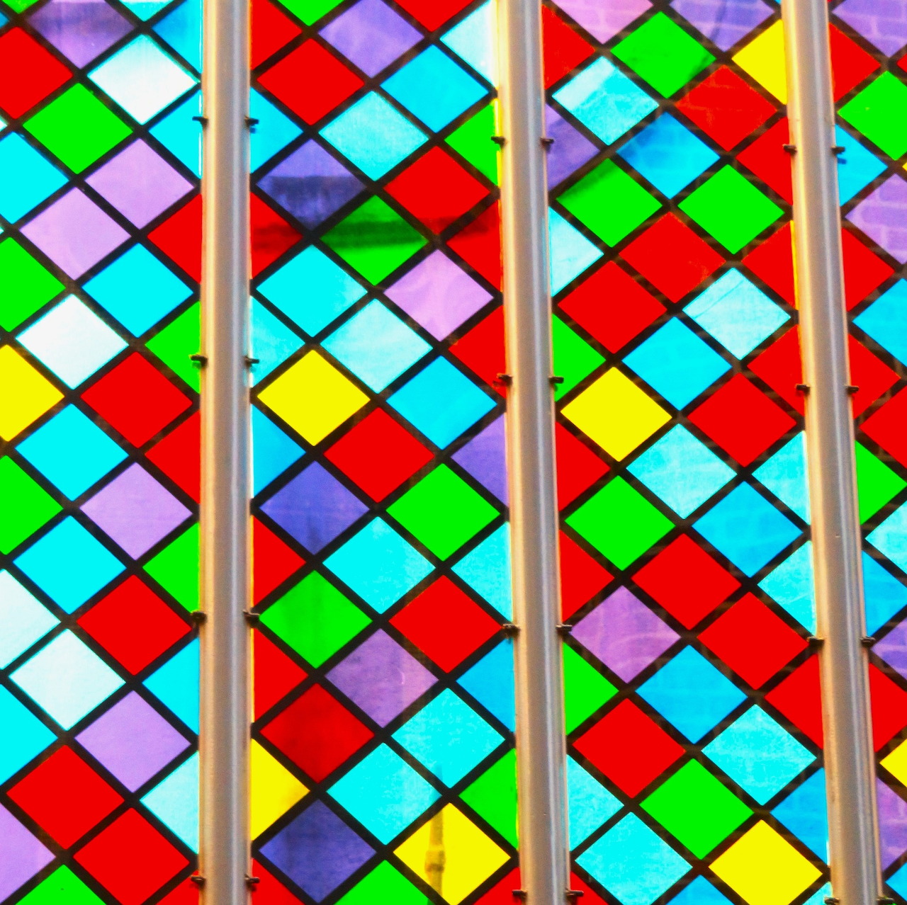 Colorful stained glass window with diamond-shaped panes in red, green, blue, purple, and yellow behind metal bars