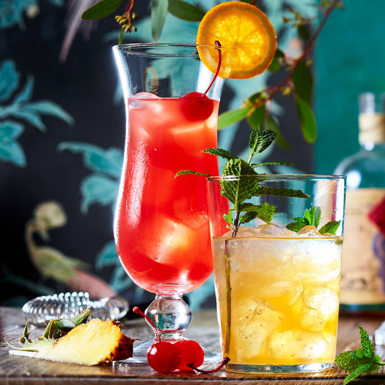 Red and yellow tropical cocktails with fruit garnish and ice on wooden table