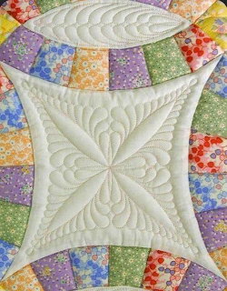 Detailed quilted fabric with cream center and colorful patchwork border showing decorative stitching patterns