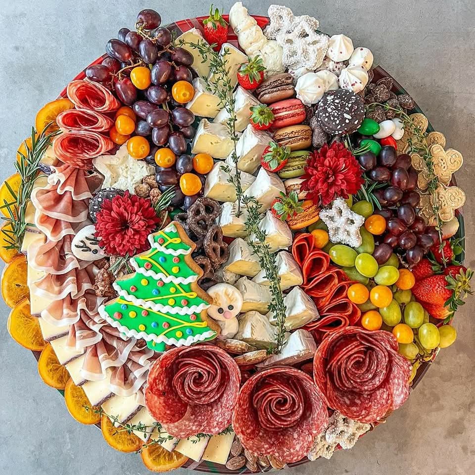 Festive circular charcuterie board with meats, cheeses, grapes, strawberries, candies, and Christmas tree cookie