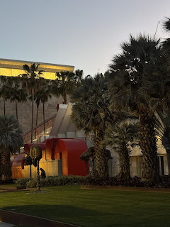 Palm trees beside a lit building and green lawn at dusk