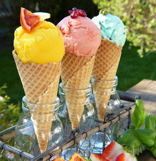 Three colorful ice cream cones with yellow, pink and blue scoops in waffle cones held in glass stands outdoors
