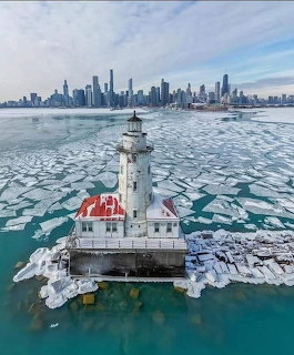 White lighthouse surrounded by ice floes with a city skyline behind it