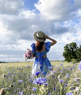 Woman in blue dress and straw hat holding pink bouquet standing in a field of purple wildflowers