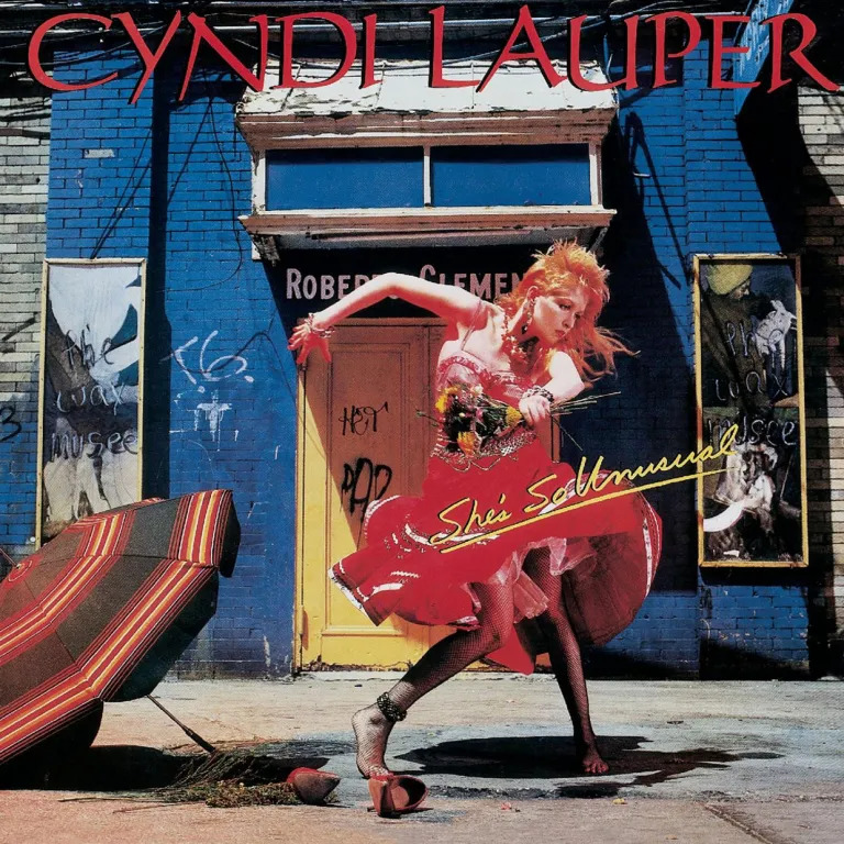 Cyndi Lauper album cover with artist in colorful outfit dancing in front of blue building